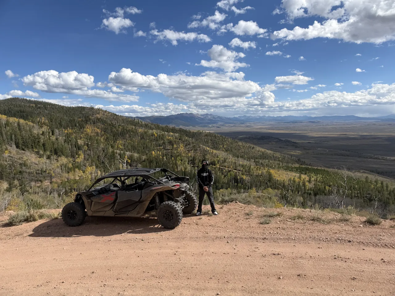 An off-road vehicle at North Sand Hills, Colorado, overlooking forest and mountains beneath a blue sky.